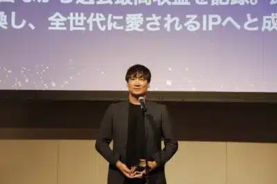 ステージ上で男性がマイクを持ち、トロフィーを掲げている