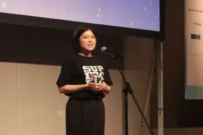 ステージ上でマイクに向かってスピーチをする女性の姿