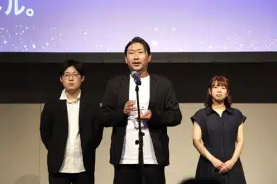 授賞式らしきイベントで、3人の男女がステージに立っている様子