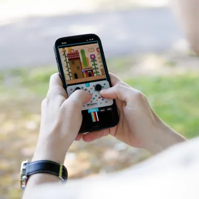 屋外でスマートフォンを操作し、ピクセルアートのレトロ風ゲームをプレイしている人物の手元