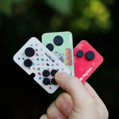 手が3枚のカード型ゲームアクセサリーを屋外で持っている様子