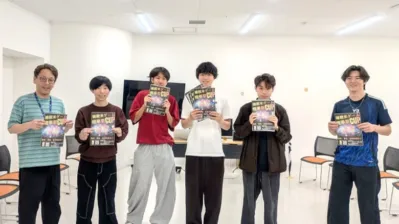 複数の男性がポスターを手に笑顔で立っている集合写真