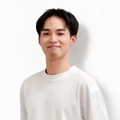 白いTシャツを着た若いアジア人男性が、白い背景の前でカメラに向かって穏やかに微笑んでいます。