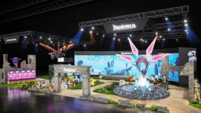 人気ゲーム「パルワールド」のイベントブースを上空から捉えた画像です。巨大なキャラクターの3Dモデルが複数展示され、背景の大型スクリーンにはゲームの世界観が映し出されています。POCKETPAIRのロゴも見え、ゲームのプロモーションイベントの様子がうかがえます。